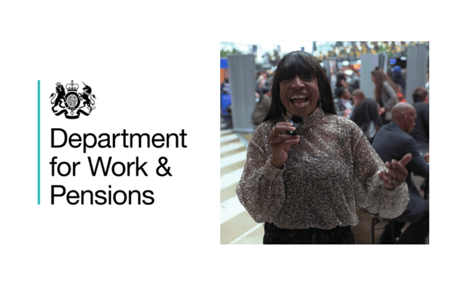 A middle aged black woman holding a mic and talking into it, wearing a light brown top.